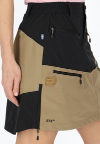 Knee-length skort featuring a color-blocked design in black and khaki, multiple zip pockets, elastic waistband, and logo patches.