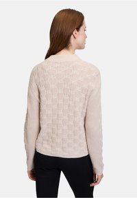 Helle beige Strickjacke mit strukturiertem Blasenmuster, ausgestattet mit einem gerippten Kragen und langen Ärmeln. Von hinten gezeigt.