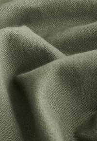 Tissu vert olive avec une surface lisse et texturée ; les plis créent des ombres douces et mettent en valeur le motif du tissage.