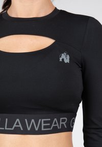 Zwarte lange mouw crop top met een uitsnijd ontwerp, een grijs logo op de borst en een donkere tailleband met de tekst "Gorilla Wear" in grijs.