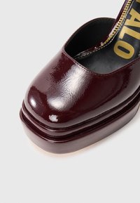 Kläbise tumepunase platvormking, millel on ruudukujuline varvas ja mustal sisetallal nähtav kuldne tekst heledal taustal.