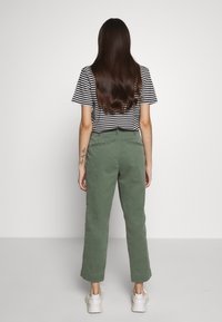 Zelené bavlněné kalhoty rovného střihu, spárované s černobílým pruhovaným tričkem. Model má na sobě bílé tenisky.