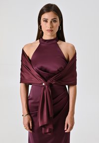 Burgundy satin dress with halter neckline and draped shawl. Features a tied detail at the waist with a pearl accent. Smooth texture.