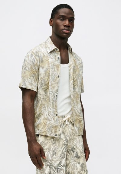 Chemise à manches courtes beige clair avec un motif de feuilles, fabriquée dans un tissu léger. Associée à un short coordonné avec un cordon de serrage.