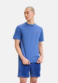 Camiseta de algodón azul con mangas cortas, cuello redondo y pequeño logo bordado en naranja, combinada con pantalones cortos de pana azul texturizados.