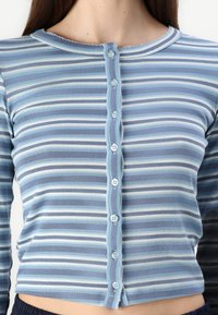 Cardigan riscado em azul claro, feito de um tecido macio, apresenta um decote redondo, bordas em forma de onda e seis botões combinando na frente.