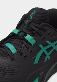 Μαύρο αθλητικό παπούτσι ASICS με τόνους τιρκουάζ, με λεπτομερή κοντινή λήψη των κορδονιών, του λογότυπου και της αναπνεύσιμης γλώσσας από δίχτυ.