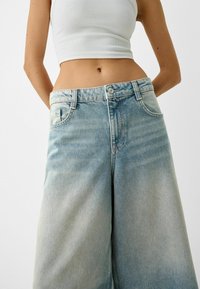 Breda ljusblå denimjeans med en urblekt finish, hög midja, framfickor och knäppning. Slät textur.