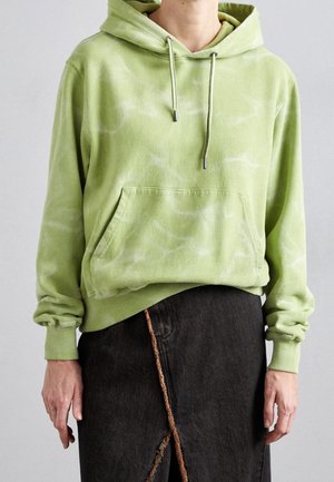 Lysegrøn tie-dye hættetrøje med lomme foran og snore, båret med en sort nederdel med en frynset skrå søm.