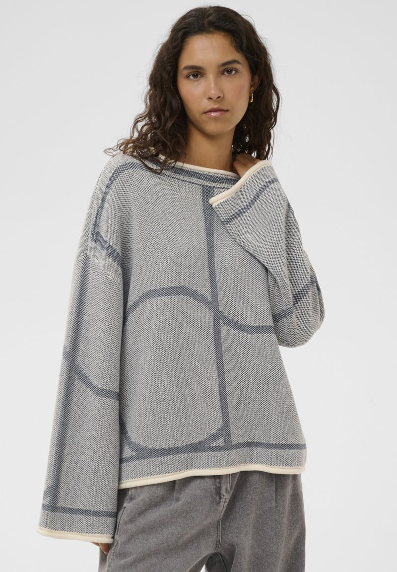 Pull surdimensionné gris et blanc avec un motif géométrique, tissu en maille texturée et encolure large. Bords garnis avec une finition douce.