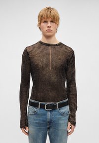 Camisola justa de manga comprida em castanho escuro com textura canelada. Apresenta decote redondo e riscas finas, usada com jeans de ganga azul e cinto preto.