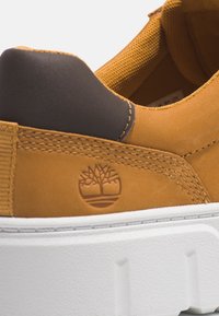Gros plan sur le talon d'une chaussure en cuir beige avec un col rembourré noir, un logo d'arbre embossé et une épaisse semelle blanche à motif texturé.