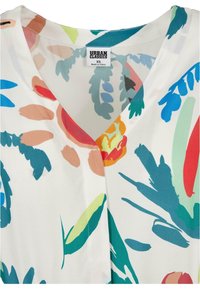 Bloes met bloemenpatroon op een witte basis, met levendige blauwe, groene, oranje en roze ontwerpen. V-hals, gladde textuur, en label zichtbaar.
