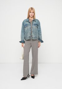 Denim jacket with light blue wash, a relaxed fit; tan striped wide-leg pants; black heeled shoes; white handbag.