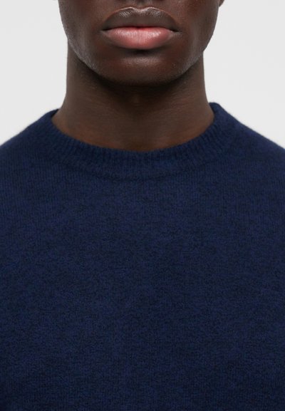 Πουλόβερ σε ναυτικό μπλε, πλεκτό με στρογγυλή λαιμόκοψη, απαλής υφής, εφαρμοστό στον λαιμό, με λεία επιφάνεια χωρίς ορατά σχέδια ή μεταλλικά στοιχεία.