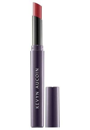 Tube de rouge à lèvres violet avec une pointe en forme de bullet rouge incurvé, mécanisme de rotation noir, et une étiquette en texte blanc portant la mention "KEVYN AUCOIN." Capuchon retiré.