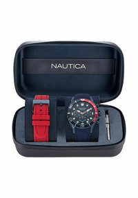 Set de reloj Nautica con correa azul marino y esfera acentuada en rojo, incluye una correa de goma roja y herramienta, todo en un estuche negro con cremallera.