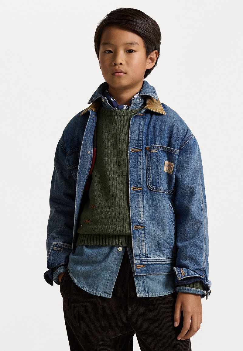 Denim jacket with brown collar over green knit sweater and blue button-up shirt. Features multiple pockets and contrasting stitching details.