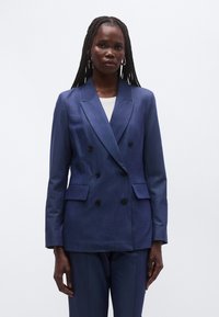 Tamsiai mėlynas dvieilis švarkas iš faktūrinės medžiagos, su dideliais atlapais ir keturiais juodais mygtukais, papildytas dviem šoniniais kišenėmis funkcionalumui.