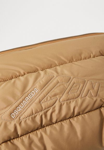 Beige vuorattu puffer-takki, jossa on näyttävä brodeerattu logo "ICON" ja "DSQUARED2", sileä, kiiltävä pinta ja näkyvä vetoketju.