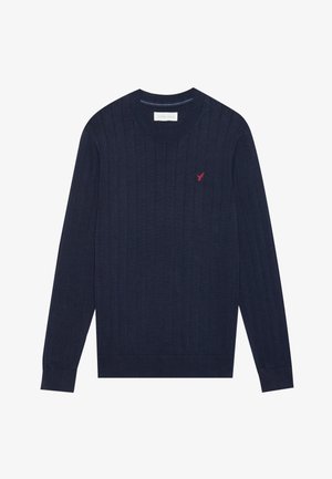 Suéter de canalé azul marino hecho de material suave, con cuello redondo y mangas largas. Presenta un pequeño logo rojo en el pecho.