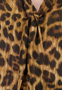 Luipaardprint blouse met een knoopdetail bij de hals. Gemaakt van een lichte stof met een glanzende textuur in tinten bruin en zwart.