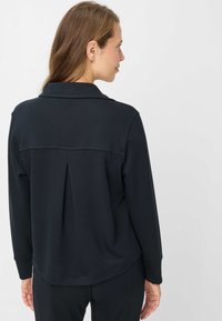 Sort, langærmet bluse med krave og detaljer med bageste plissé, lavet af glat stof, med en afslappet pasform og diskrete syninger.