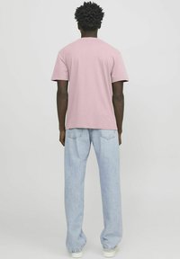 Rosa Baumwoll-T-Shirt mit Rundhalsausschnitt, kurzen Ärmeln und lockerer Passform, kombiniert mit hellblauen Denim-Jeans und weißen Schuhen.