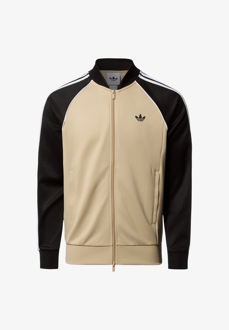 Beige and black zip-up jacket with three white stripes on sleeves, featuring a high collar and iconic logo on the chest. Fabric: smooth texture.