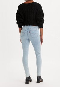 Suéter corto de punto trenzado negro, jeans ajustados azul claro con bolsillos traseros, combinado con botines negros de tacón. Textura de tela suave.