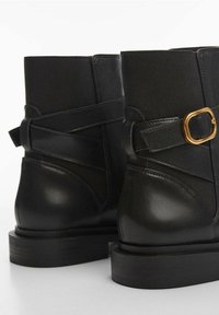 Zwarte enkellaarzen met een combinatie van leer en canvas, met een gouden gespsluiting en een dikke, gestructureerde zool.