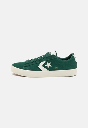 Baskets basses en daim vert avec étoile blanche et logo Chevron sur le côté, semelle blanche, lacets verts et "CONS" imprimé en doré près du talon.