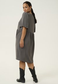 Vestido gris con mangas cortas y flotantes, cintura elástica y falda fluida. Combinado con botas vaqueras negras con detalles grabados.