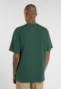 Zelené bavlněné tričko s krátkými rukávy, kulatým výstřihem a volným střihem. Obsahuje štítek na lemu a má hladkou texturu.