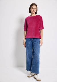 Top corto a maniche corte in corduroy magenta con scollo ampio, abbinato a jeans in denim azzurro chiaro a gamba larga e sneakers bianche.