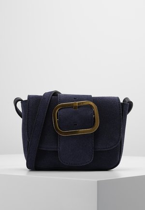 Bolso cruzado de ante azul marino con solapa rectangular, hebilla dorada oversized y correa ajustable. Superficie texturizada.