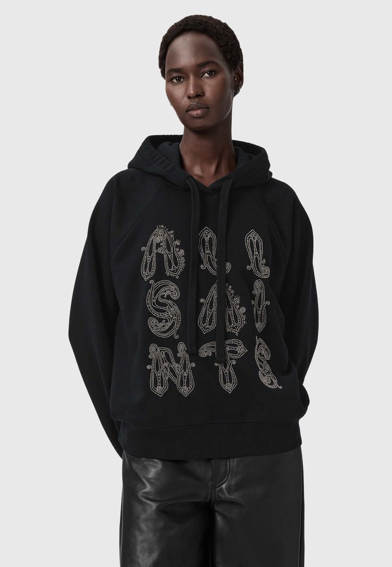 Czarna bluza z kapturem z troczkami, z ozdobnym srebrnym napisem na przodzie. Modelka ma na sobie czarne skórzane spodnie.