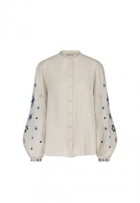 Knopenblouse van crèmekleurige stof, met ballonmouwen en borduursel van blauwe, zwarte en gouden sterren. Zachte textuur met een ronde kraag.