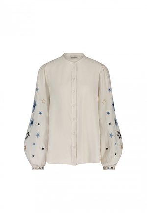 Knopenblouse van crèmekleurige stof, met ballonmouwen en borduursel van blauwe, zwarte en gouden sterren. Zachte textuur met een ronde kraag.