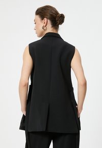 Blazer senza maniche nero con un colletto affilato, vestibilità sartoriale e tasche laterali. Tessuto morbido con un'apertura sul retro.