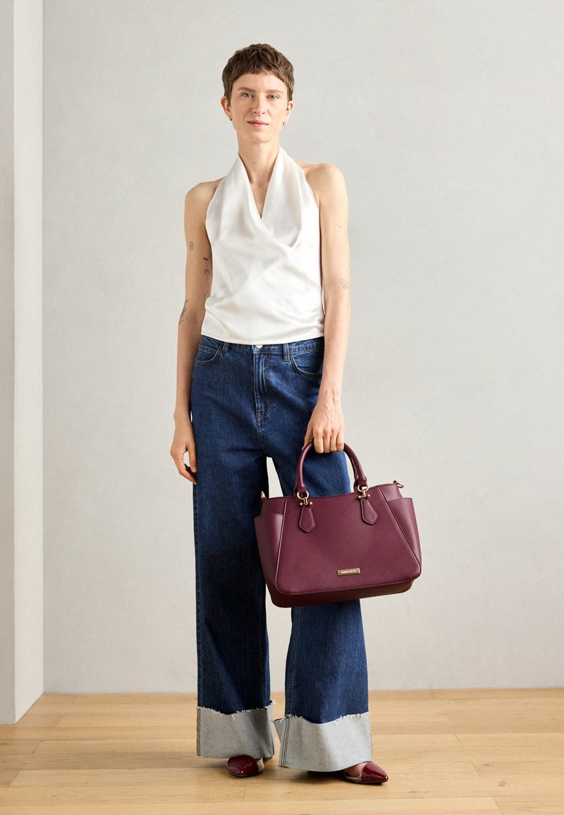 Top halter blanco, jeans sueltos azules con puños grises contrastantes, bolso de cuero burdeos con herrajes dorados y zapatos burdeos a juego.