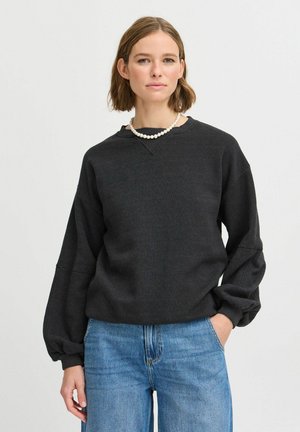 Dunkelgrauer Pullover mit lockerer Passform, Rundhalsausschnitt und überschnittenen Schultern. Kombiniert mit hellblauen Jeans.