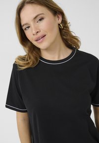 Sort kortærmet t-shirt med rund hals, med en hvid piping-detalje langs halsudskæringen ogærmerne, lavet af glat stof.