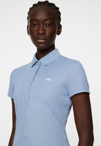 Jasnoniebieska koszulka polo z teksturowanym wzorem, krótkimi rękawami i kołnierzykiem. Posiada białe logo na piersi.