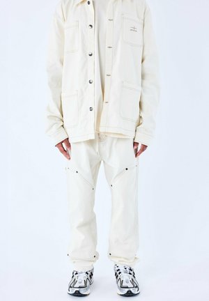 Giacca oversize color crema con tasche frontali, chiusura a bottone e cuciture a contrasto, abbinata a pantaloni coordinati con tasche con cerniera.