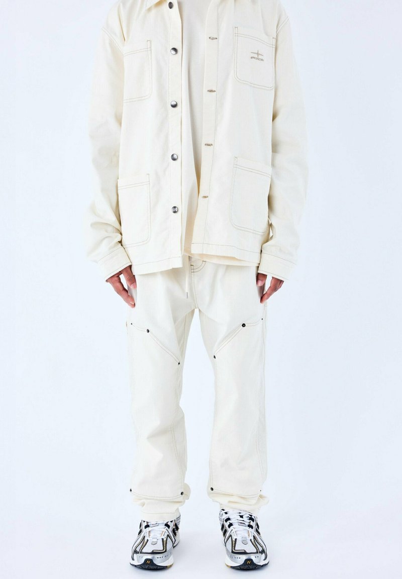 Veste surdimensionnée crème, avec poches avant, fermeture à boutons et couture contrastante, assortie à un pantalon à poches zippées.