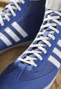 Blå sportskor tillverkade av syntetiskt material med vita detaljer, utrustade med en texturerad yta, perforeringar och vita skosnören.