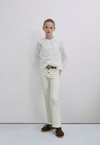 White long-sleeve shirt with large embroidered collar, paired with off-white jeans and brown lace-up shoes. Simple, contemporary design.