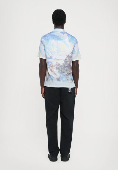 Short-sleeve, light blue shirt with a detailed artistic print on the back; paired with black pants; smooth fabric texture.