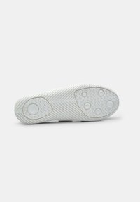 Suela de zapato de goma blanca con un patrón en zigzag, detalles de agarre circulares y una superficie texturizada para tracción. Diseño plano sin marcas visibles.